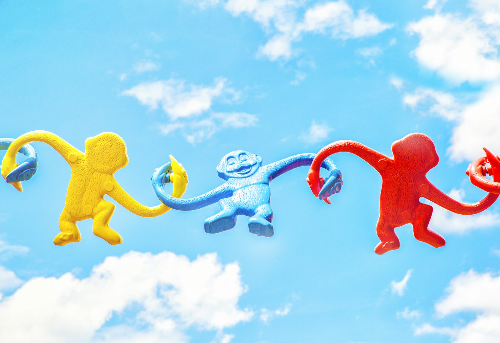 photo of three toy monkeys kind of holding hand together, the background is a bright blue sky with a few clouds